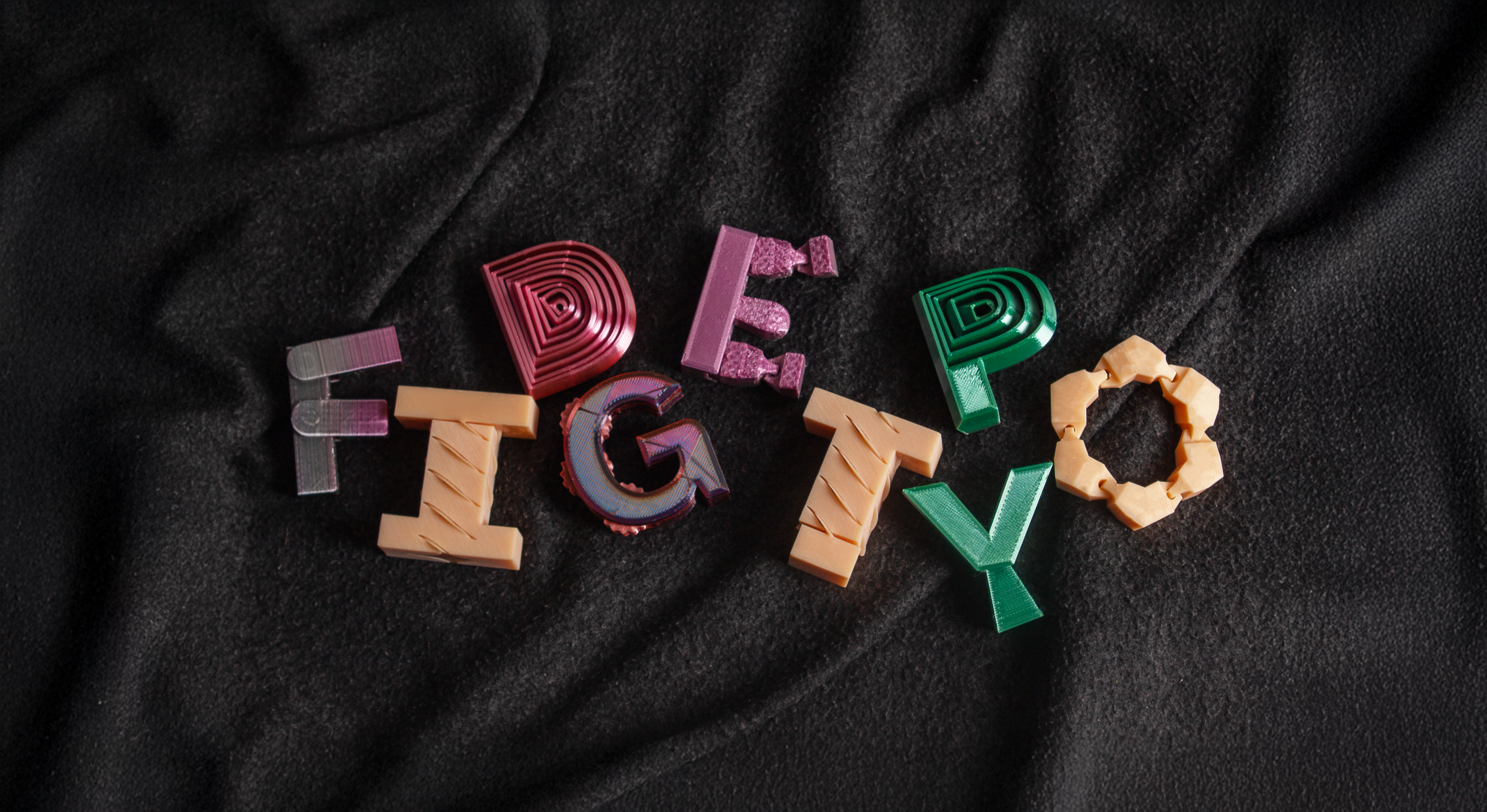 Letter-shaped 3D printed fidget toys spelling the name of the project: FIDGETYPO